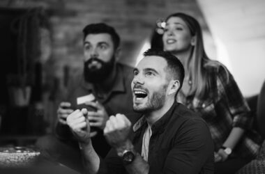 young man cheering his team while watching sports championship with friends